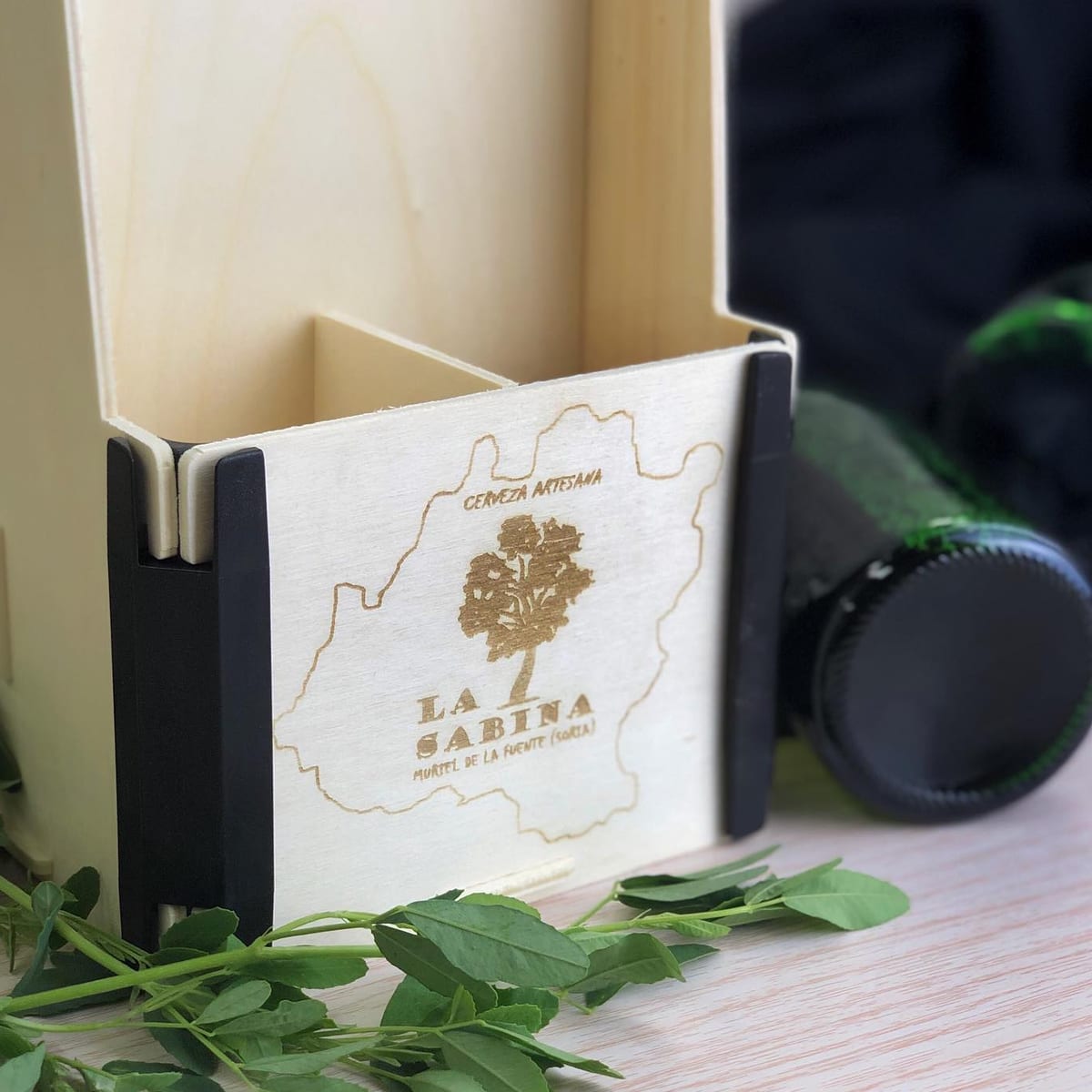 Caja con asa para cuatro botellines con el logo de una cervecera artesana grabado en el frontal y esquineras negras