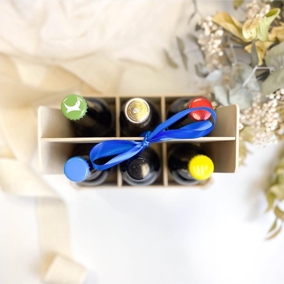 Pack de madera Sincla con asa para seis botellas de cerveza visto desde arriba, con chapas de colores y un lazo azul