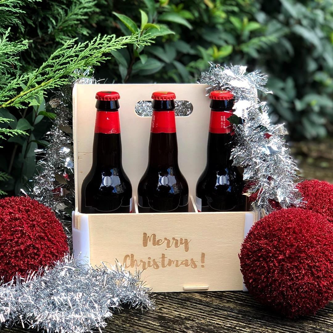 Caja con asa para seis cervezas con «Merry Christmas!» grabado, con tres botellas, espumillón y bolas rojas