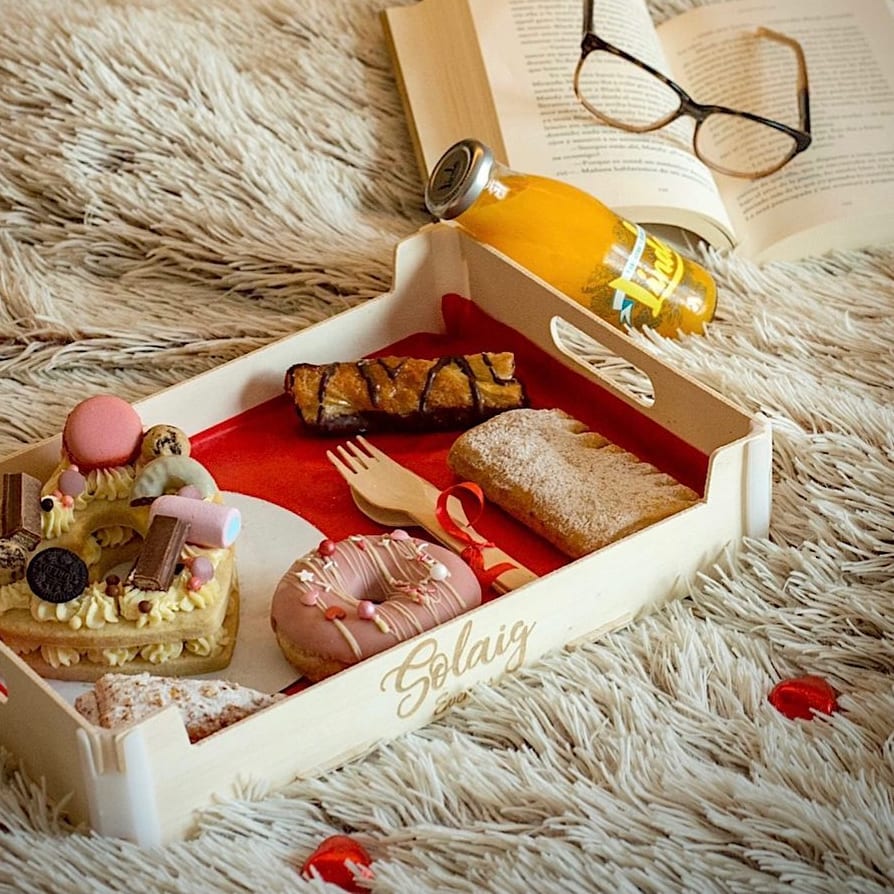Holztablett mit dem eingravierten Namen eines Frühstücksdienstes, mit Süßem, Donut und Saft, auf einer flauschigen Decke