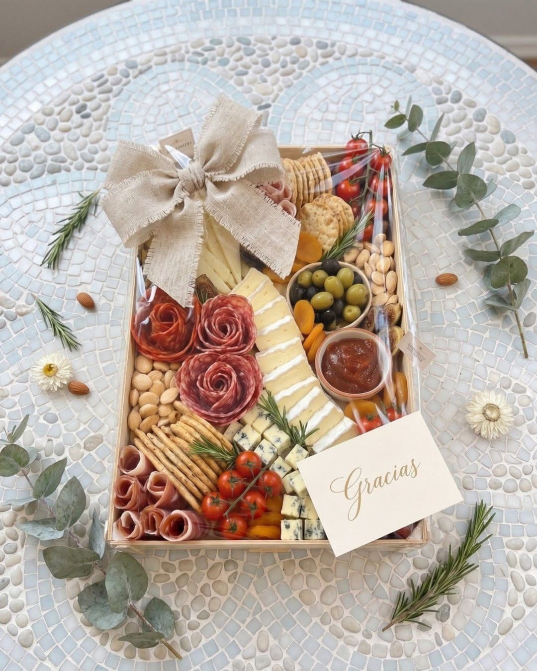 Sincla-Holztablett mit Wurst, Käse, Kirschtomaten und Crackern, in Zellophan verpackt, mit Leinenschleife und einer „Gracias“-Karte