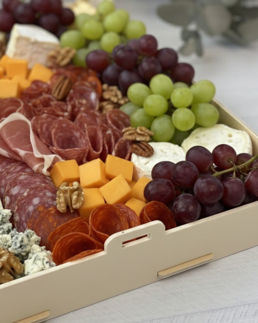 Bandeja de madera con asas llena de quesos, embutidos, uvas y frutos secos