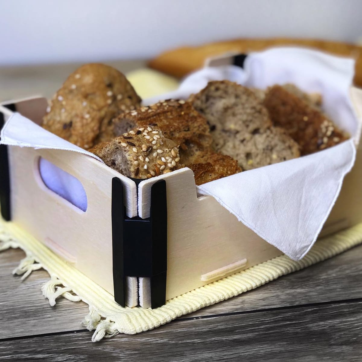 Holzkorb mit schwarzen Eckverbindern und weißer Serviette, voller Brot und Brötchen