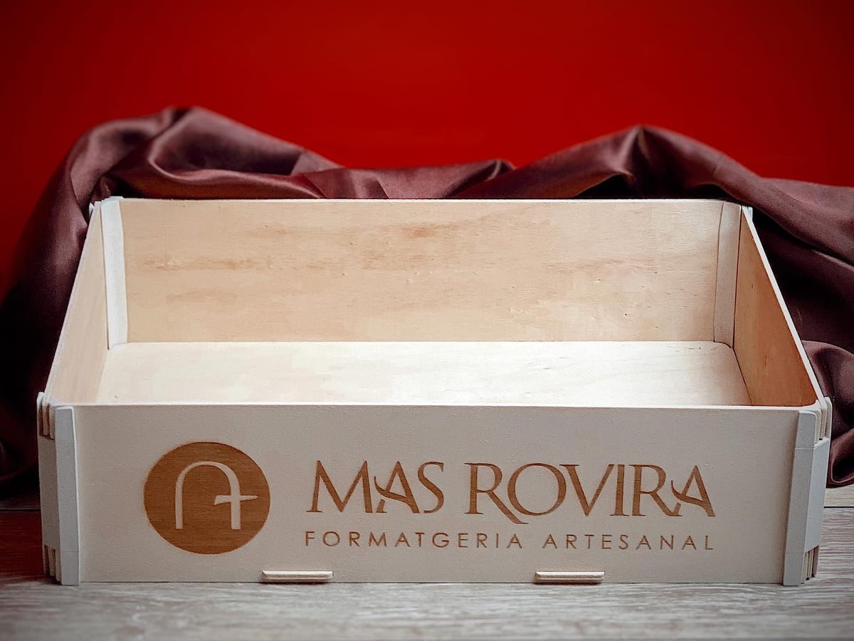 Boîte en bois sans couvercle avec le logo et le nom d’une fromagerie artisanale gravés sur la face avant, sur fond rouge