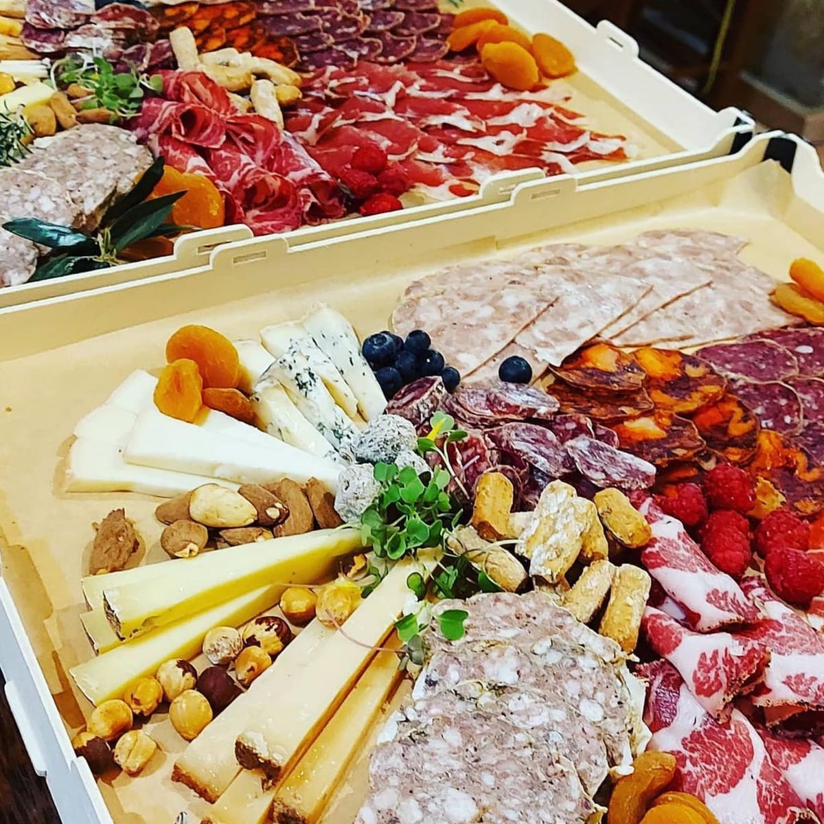 Boîtes sans couvercle remplies de fromages, de charcuterie, de fruits secs et de fruits, prêtes pour une dégustation
