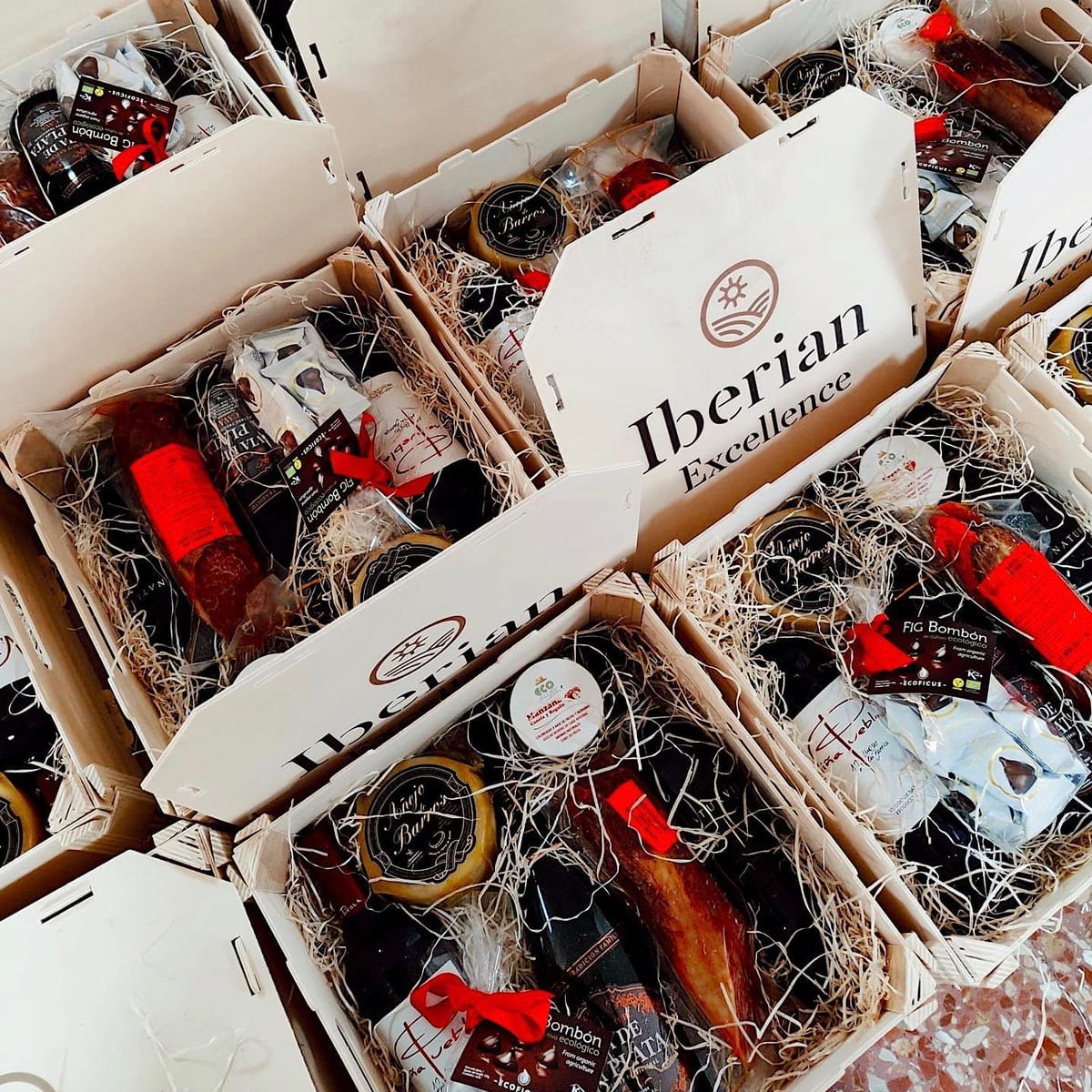 Dutzende offene Holzkisten mit Firmen-Weihnachtspräsenten (Käse, Wurst, Süßes und Wein) auf Füllmaterial, mit dem Kundenlogo auf den Deckeln