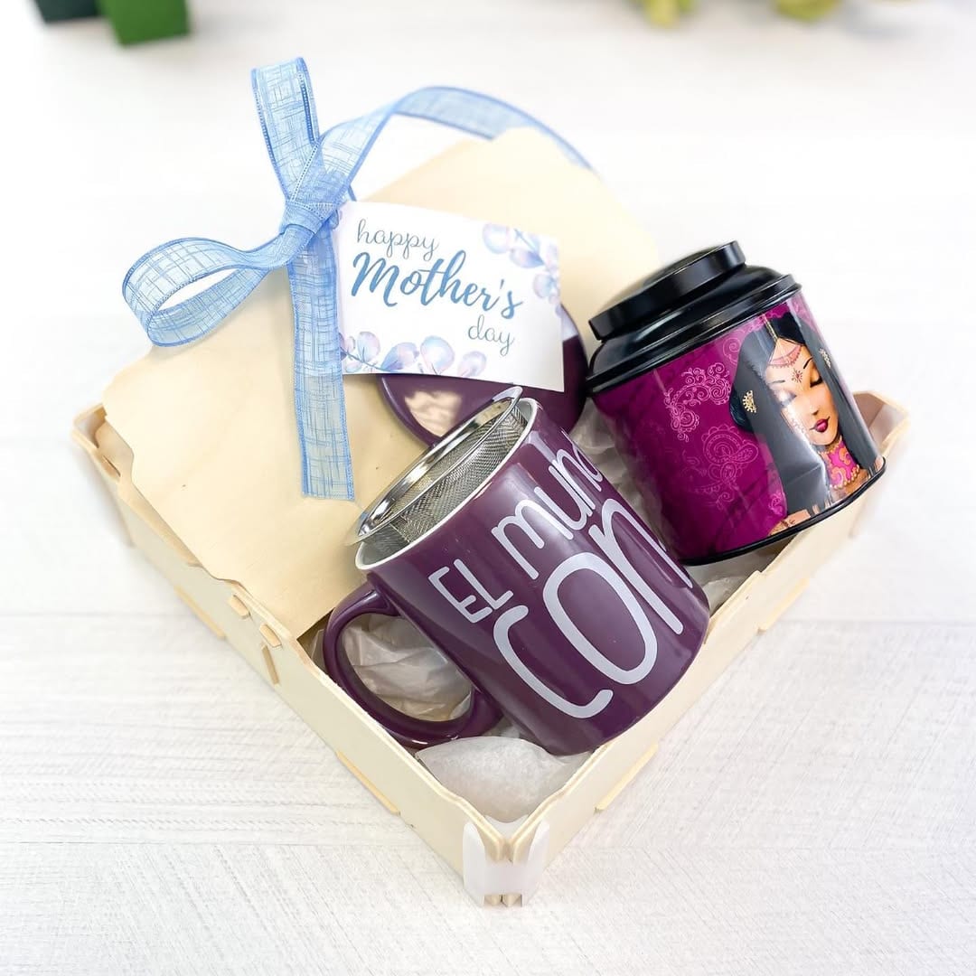 Scatola con una tazza viola con infusore e una latta di tè, con un’etichetta della festa della mamma e un nastro azzurro