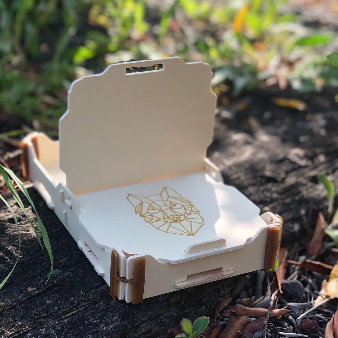 Petite boîte ouverte avec une illustration géométrique de renard gravée au fond, sur de la terre et des feuilles