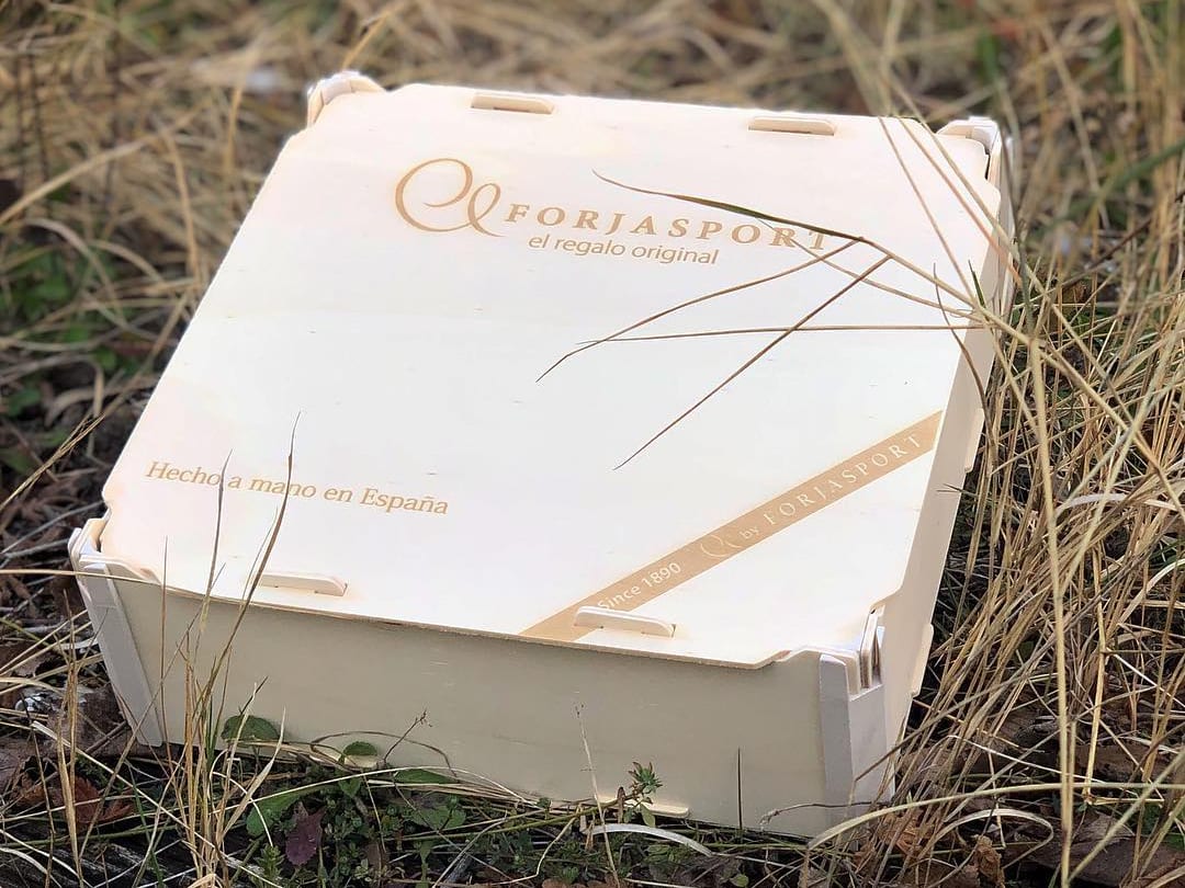 Boîte en bois avec couvercle gravée du logo d’un atelier de ferronnerie et de « Hecho a mano en España » (fait main en Espagne), sur de l’herbe sèche