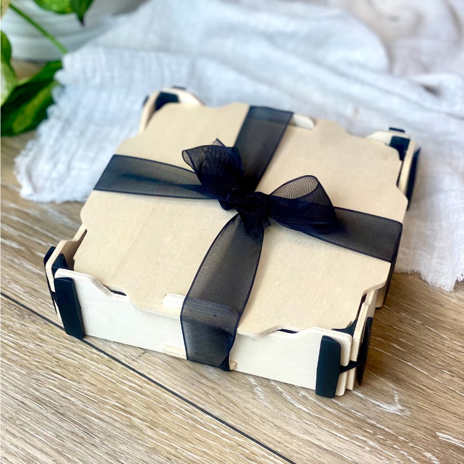 Boîte avec couvercle et coins noirs nouée d’un ruban d’organza noir, sur une table en bois