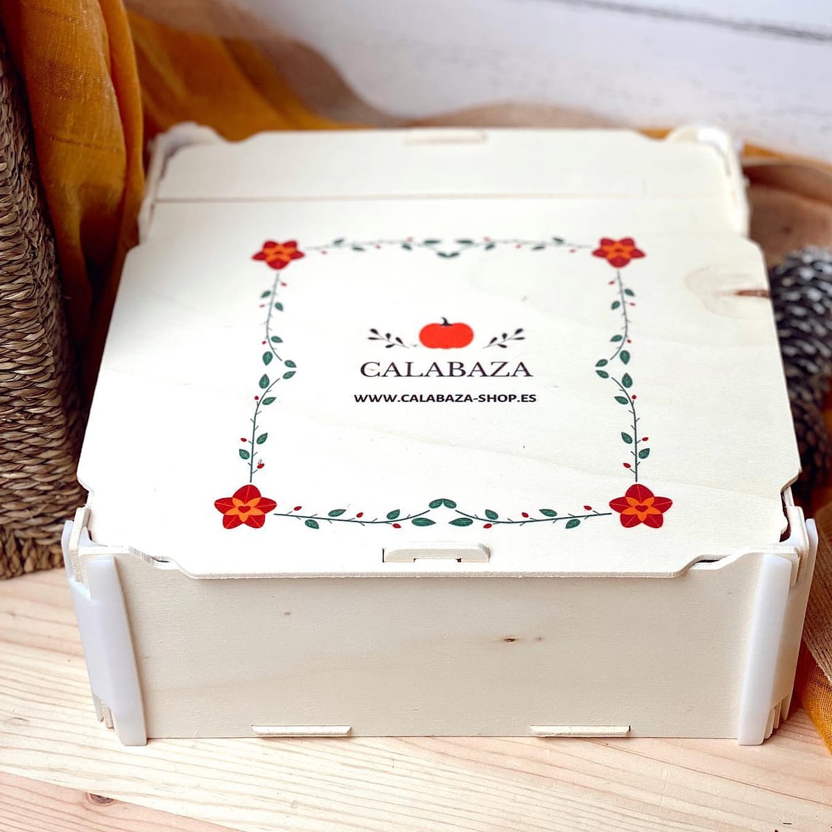 Boîte avec couvercle imprimée en couleur au logo d’une boutique de cadeaux, entouré d’un cadre de fleurs rouges et de feuilles vertes