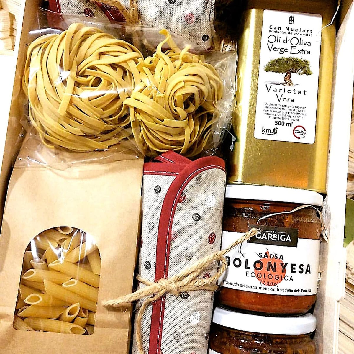 Italienisches Kochset in einer Holzkiste: frische Pasta, Makkaroni, Olivenöl, Bolognese-Sauce und ein Topfuntersetzer aus Stoff