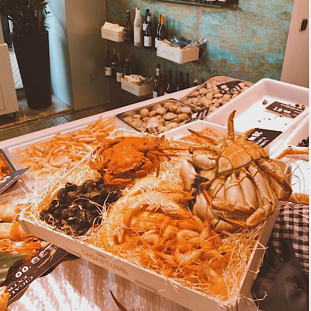 Holzkiste mit Holzwolle voller Seespinnen, Garnelen, Kaisergranat und Miesmuscheln, auf der Theke eines Fischrestaurants