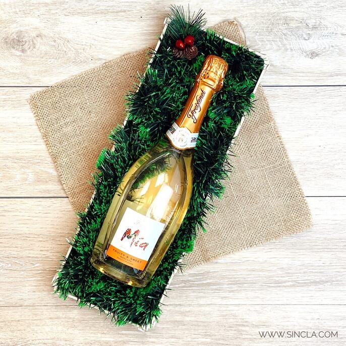 A bottle of cava lying in a wooden box with green tinsel, on hessian