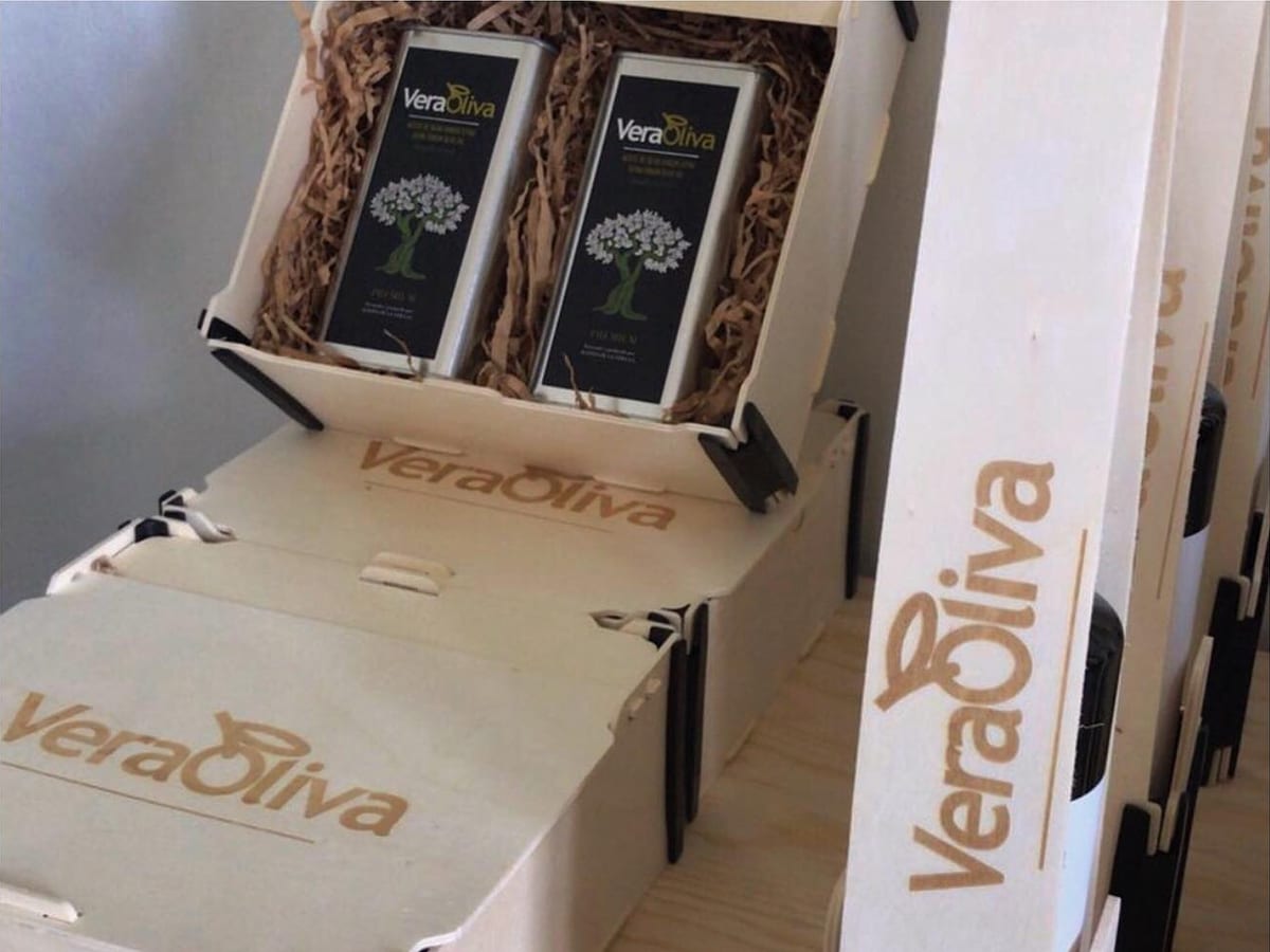 Caja con dos latas de aceite y tapas con el logo de la marca grabado, junto a una caja para una botella vertical con el mismo logo