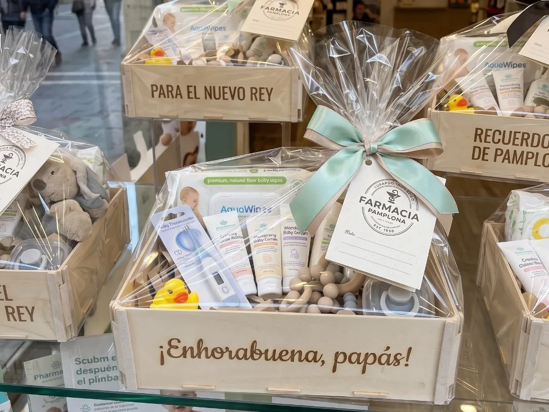 Babyset in einer Holzkiste mit der Gravur „Herzlichen Glückwunsch, liebe Eltern!“ vorne, in Zellophan mit grüner Schleife und dem Etikett der Apotheke