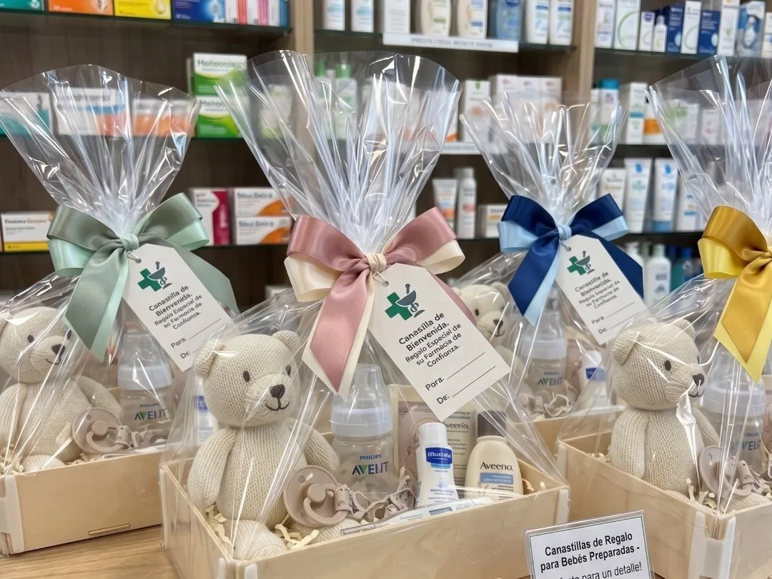 Babysets in Holzkisten ohne Deckel, in Zellophan verpackt, mit grünen, rosa, blauen und gelben Schleifen und einem Teddybären, in einer Apotheke