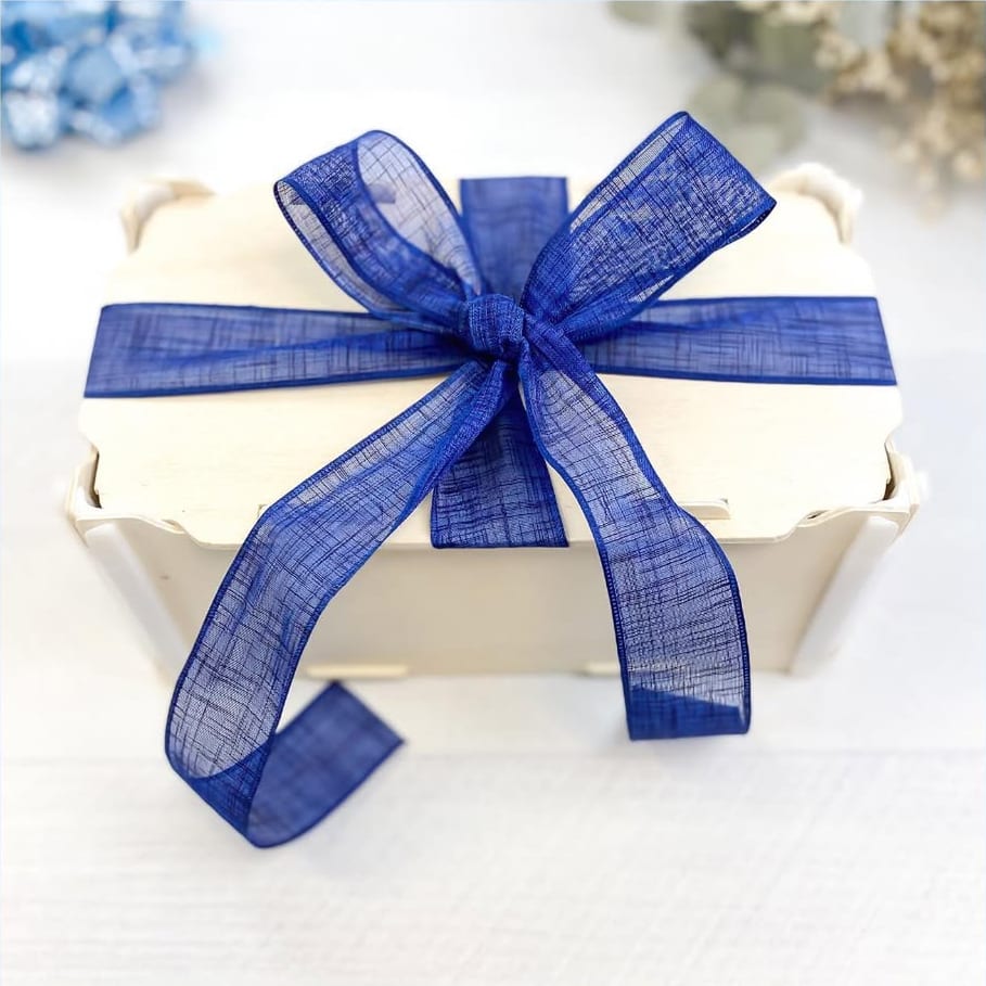 Caixa de madeira com tampa atada com um grande laço de organza azul-marinho, sobre uma mesa branca