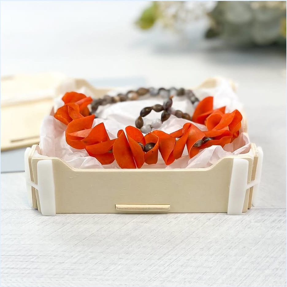 Caja baja de madera abierta con un collar artesanal de pétalos naranjas sobre papel de seda