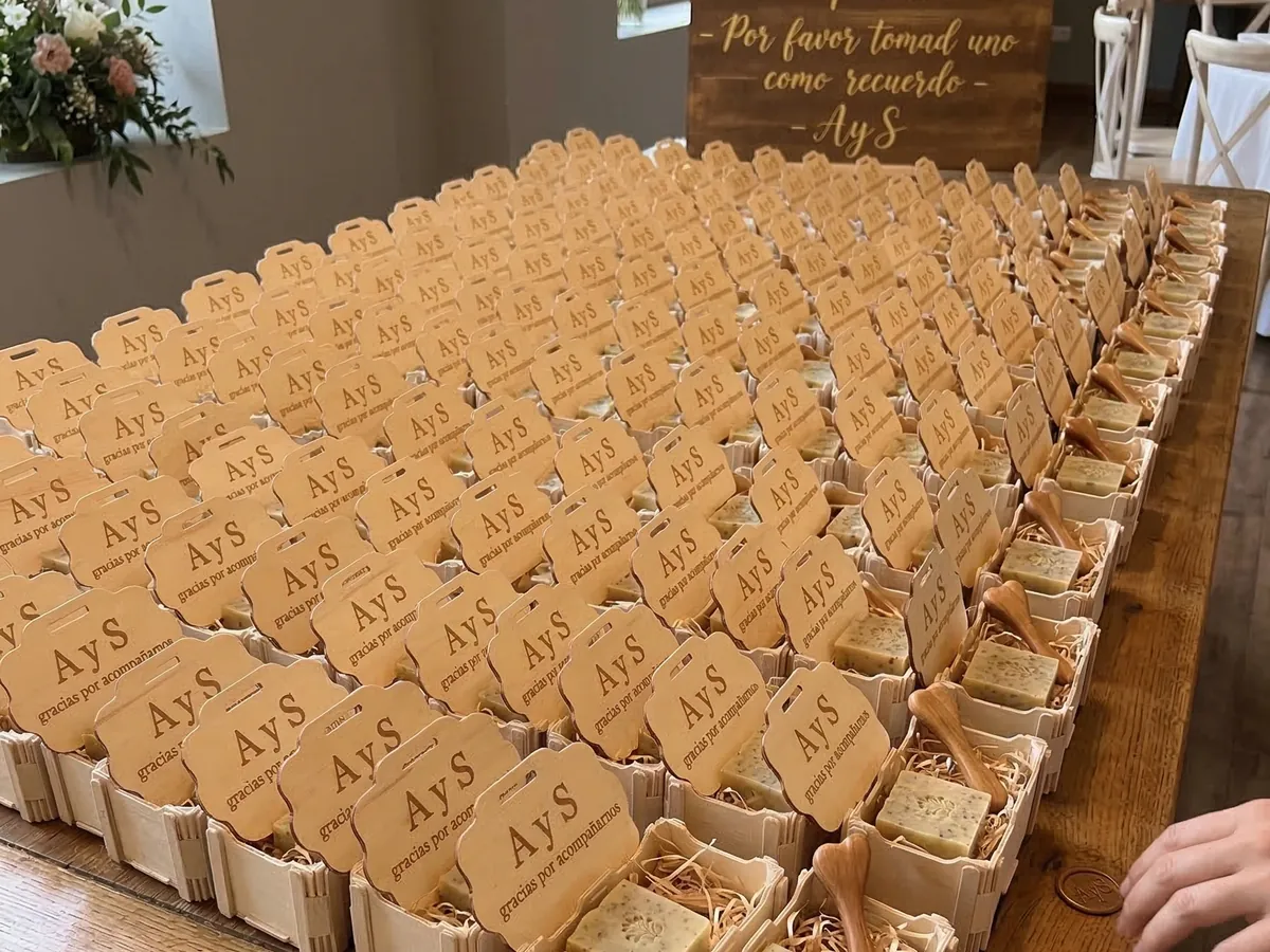 Mesa larga con decenas de cajitas de madera con las iniciales de los novios grabadas, cada una con un jabón, y un cartel de «Gracias por acompañarnos»