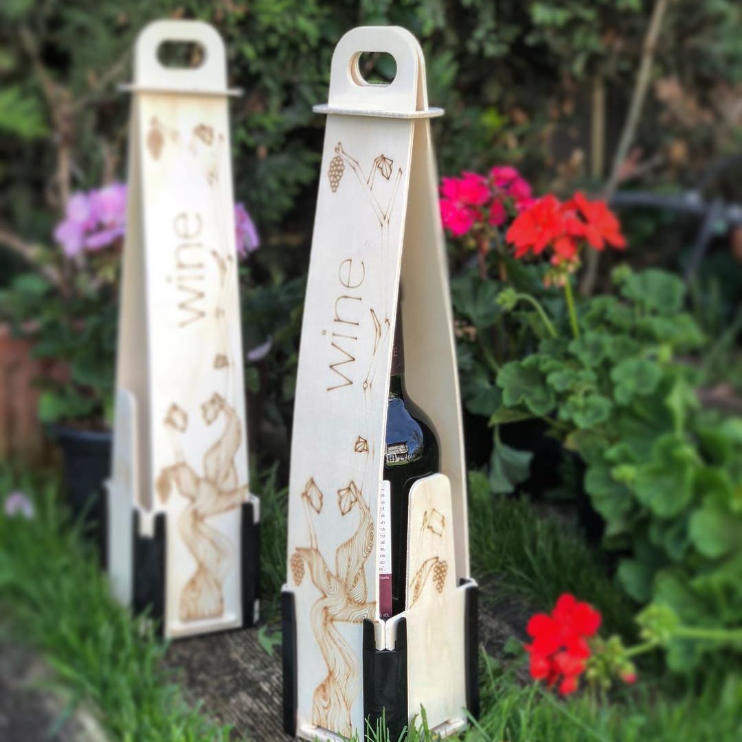 Two wooden vertical bottle boxes with a handle, the word “wine” and vine leaves engraved, among flowers